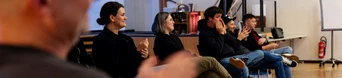 A group of six people seated in a room, some clapping, engaged in a discussion or presentation.