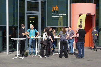 Groups of people engage in conversation outside SRH University, with tables set up for a gathering or event.
