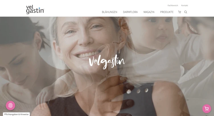 Lächelnde Frau, die ein Baby hält, mit einer anderen Frau im Hintergrund. Der Text "Velgastin" ist deutlich sichtbar.