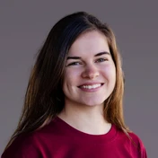 Young woman with long brown hair, wearing a maroon shirt, smiling against a neutral background.