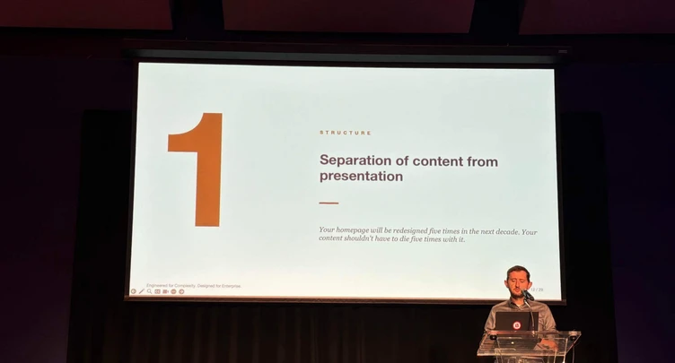A speaker presents on stage, discussing the separation of content from presentation, with a slide displaying the number "1" and key points.