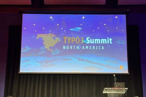 Präsentationsbildschirm, der 'TYPO3 Summit Nordamerika' mit einem blauen aquatischen Hintergrund und einem Podium davor anzeigt.