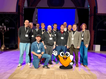 Group of twelve individuals posing together on stage, with a cartoon character in front, during an event in Utrecht.