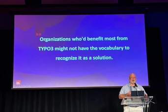 Ein Redner präsentiert auf der Bühne mit einer Folie, auf der steht: "Organisationen, die am meisten von TYPO3 profitieren könnten, haben möglicherweise nicht das Vokabular, um es als Lösung zu erkennen.