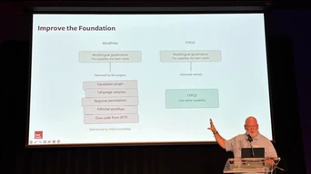 Ein Redner präsentiert auf der Bühne und spricht über mehrsprachige Governance sowie die Funktionen von WordPress und TYPO3, mit einer Folie mit dem Titel "Die Grundlage verbessern.