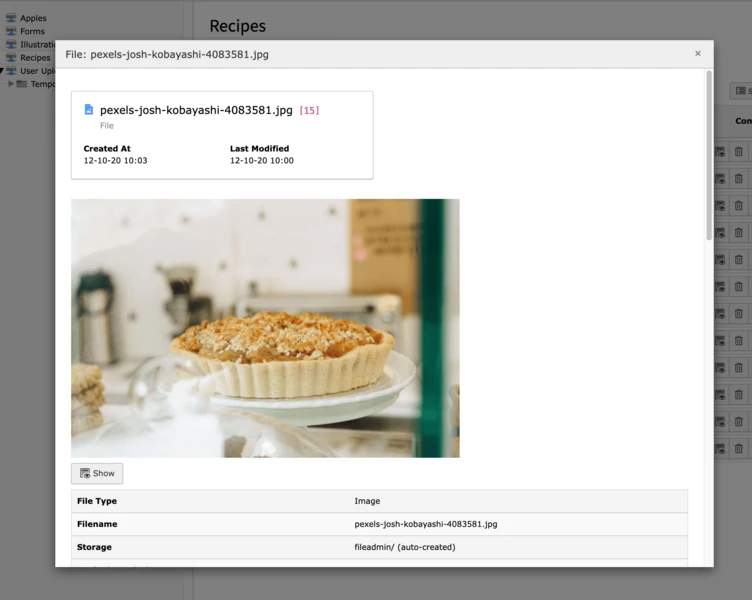 A freshly baked pie with a crumbly topping sits on a white plate, placed on a table with a blurred background of kitchen utensils and decor.